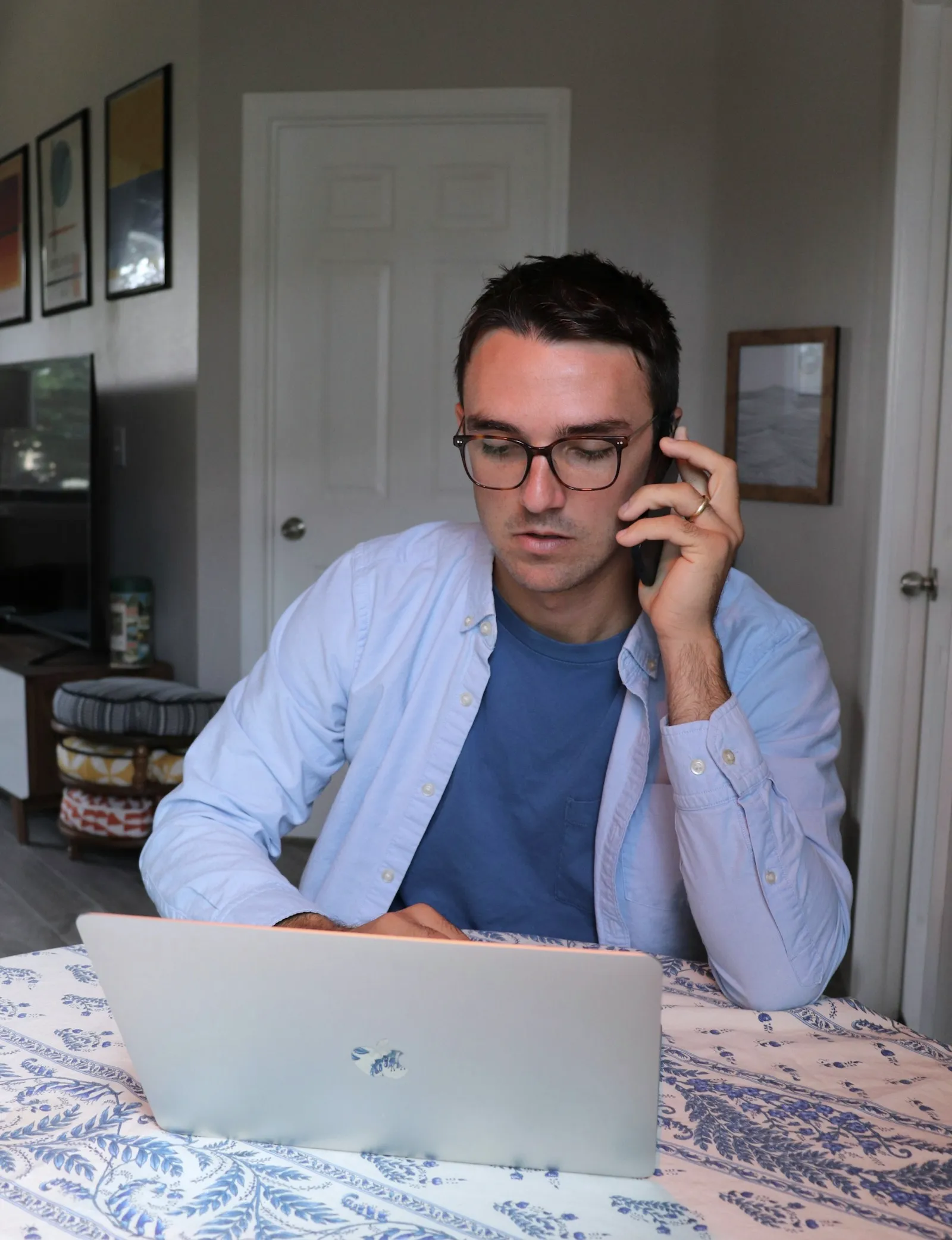 A man in glasses on a phone call at his laptop.